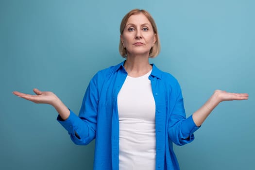 surprised blond mature woman in disbelief on blue background with copyspace.