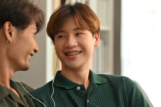 Smiling homosexual couple listening to music on the earphones and relaxing at home. LGBT, relationship and comfort living concept.