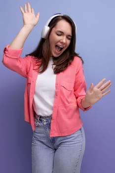 optimistic dancing brunette young woman in a shirt and jeans listens to her favorite music on headphones.