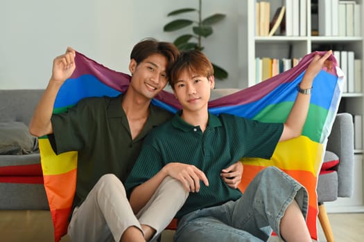 Image of gay couple embracing under LGBT pride flag. LGBT, love and human rights concept.