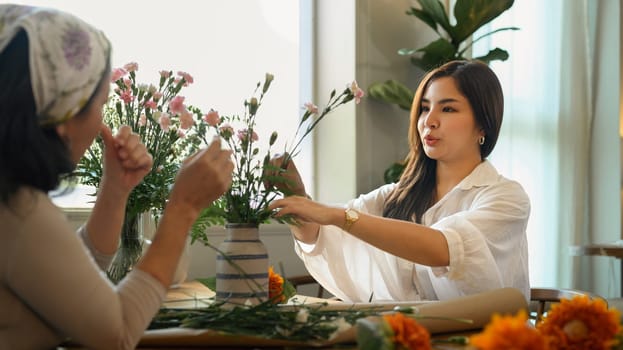 Pretty young asian woman and her senior mother making a bouquet with fresh flowers at floral shop. Small business concept.