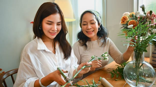 Shot of happy senior woman and adult daughter creating beautiful bouquet at home. Family and leisure activity concept.