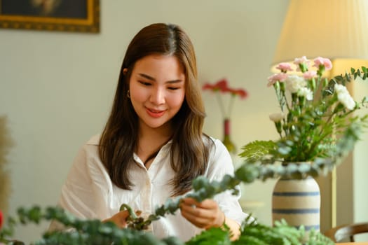 Attractive asian female florist creating beautiful bouquet with different flowers at her floral shop. Small business concept.