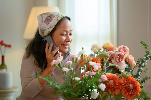 Smiling senior woman flower shop owner taking orders from client on mobile phone. Floristry and small business concept.