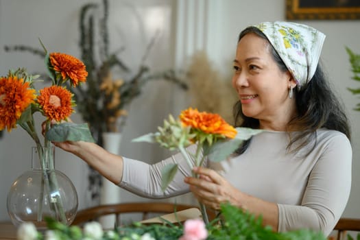 Beautiful senior woman arranging flowers in vase at her floral shop. Floristry, small business and people concept.