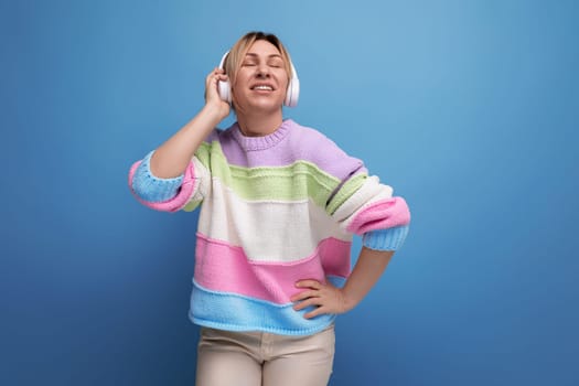 cute blond woman in a striped sweater in big headphones without a wire enjoys a song on a blue background.