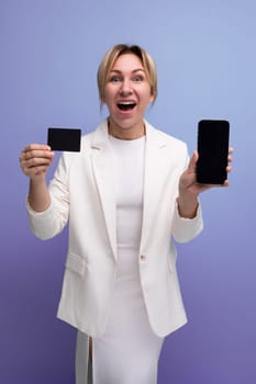 pretty slim young caucasian blond lady in a white jacket and dress holds a bank plastic card mockup.