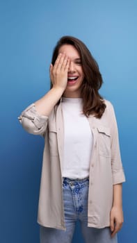 well-groomed smiling brunette 30 year old female person is dressed in a shirt and jeans on a blue background.