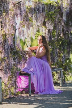 Woman wisteria lilac dress. Thoughtful happy mature woman in purple dress surrounded by chinese wisteria.