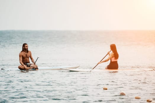 Sea woman and man on sup. Silhouette of happy young woman and man, surfing on SUP board, confident paddling through water surface. Idyllic sunset. Active lifestyle at sea or river