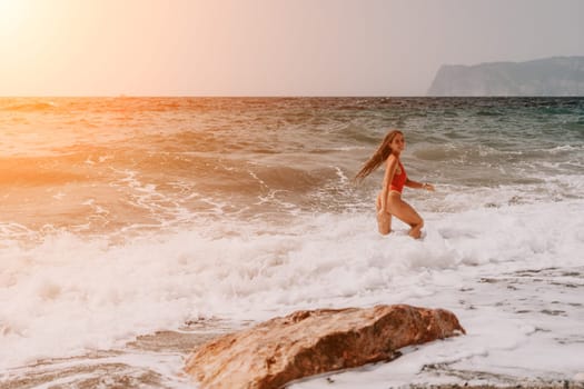 Woman travel sea. Young Happy woman in a long red dress posing on a beach near the sea on background of volcanic rocks, like in Iceland, sharing travel adventure journey