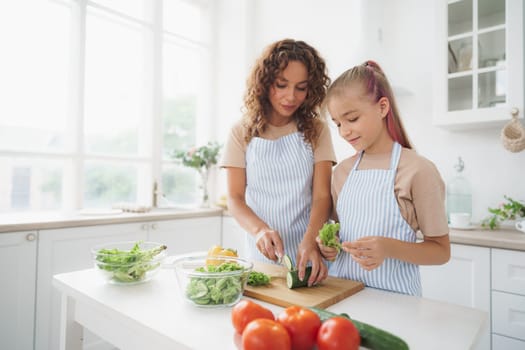 Mommy teaching her teen daughter to cook vegetable salad in kitchen, close up