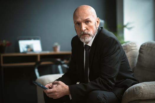 Sad man in a black suit who is looking for job. The mature businessman, with his distinguished silver beard, can be seen browsing the internet in search of work. High quality photo