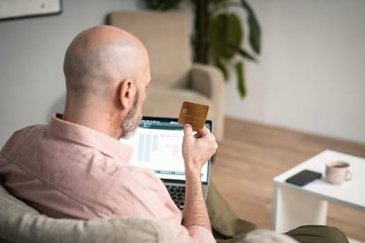 Old man make payment online. Back view, mature man holding credit card and mobile phone. Convenience and accessibility of conducting digital payments for individuals of all ages, including elderly. . High quality photo