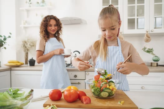 Mommy teaching her teen daughter to cook vegetable salad in kitchen, close up