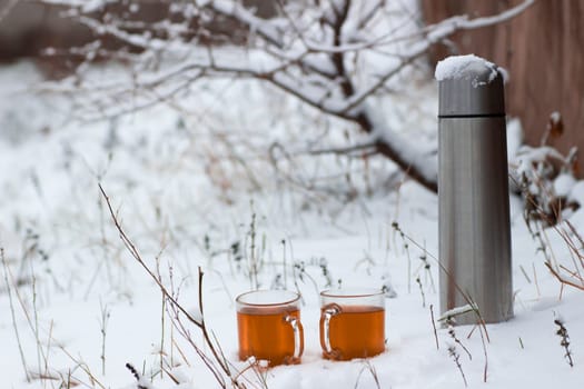 Two cups with hot tea and thermos on a  snow background