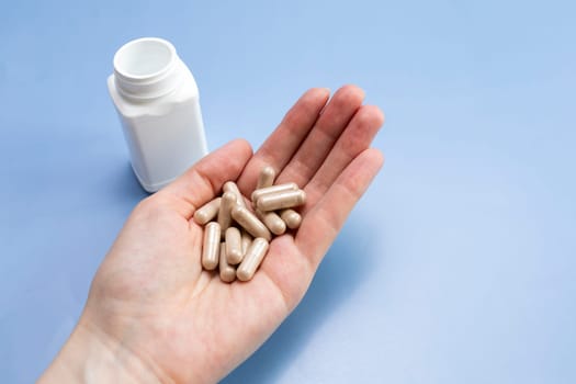 A Handful Of Pills, Softgel Capsules Of Slippery Elm On Human Hand, White Bottle ON Blue Background. Top view Dietary Nutritional Supplement, Medication. Herbal Remedy. Horizontal, Copy Space For Text.