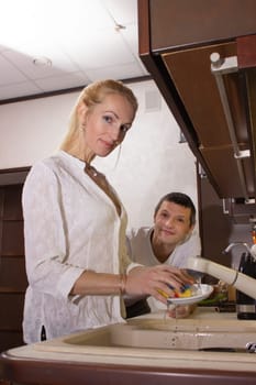 Young girl washing dishes on the kitchen, man looks