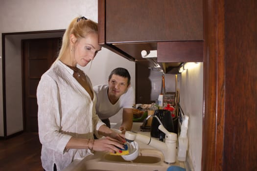 Young girl washing dishes on the kitchen, man looks