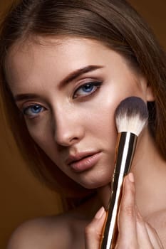 close-up, young woman applying blush on cheeks with make-up brush on beige background