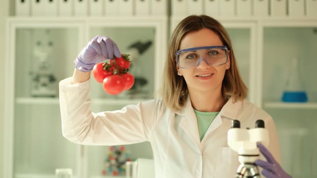 Scientist chemist in protective glasses holding branch of tomatoes in hands in chemical laboratory. Genetically modified food production concept