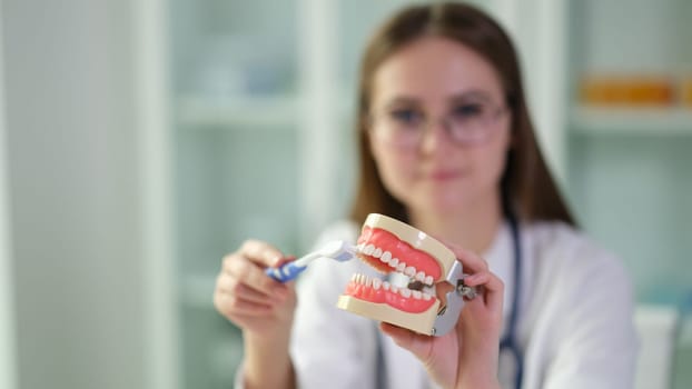 Doctor showing artificial model of human jaw and toothbrush for prevention of caries closeup. Oral care and hygiene concept