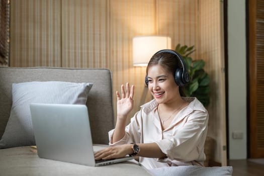 Young happy smiling woman in casual clothes sitting on sofa work online talk by video call with laptop pc computer wave hand rest relax indoors at home People lifestyle leisure concept.