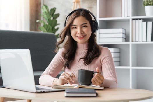 Beautiful asian woman relaxing using laptop computer while sitting on table with coffee, concept at home.