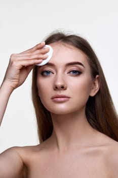 young woman holding white cotton pad for removing makeup isolated on white background