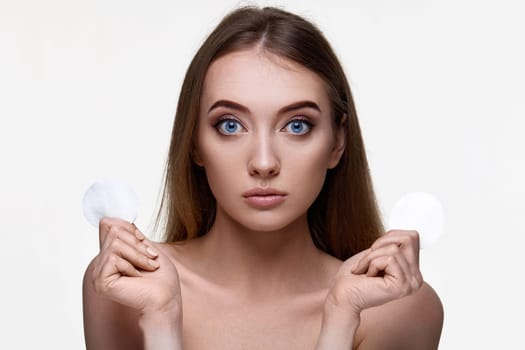 adorable woman holding two white cotton disks pad with micellar water on white background