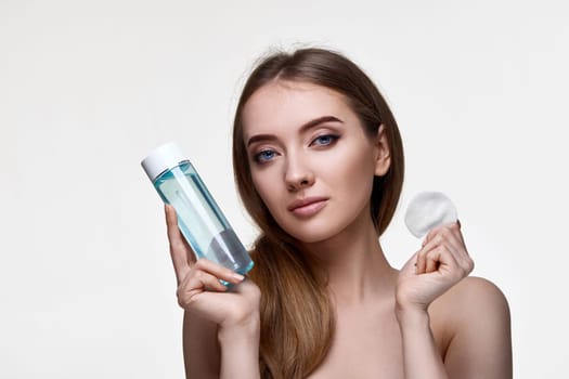 beautiful woman holding bottle with tonic, cleaning skin with cotton pad. Beauty and skin care concept