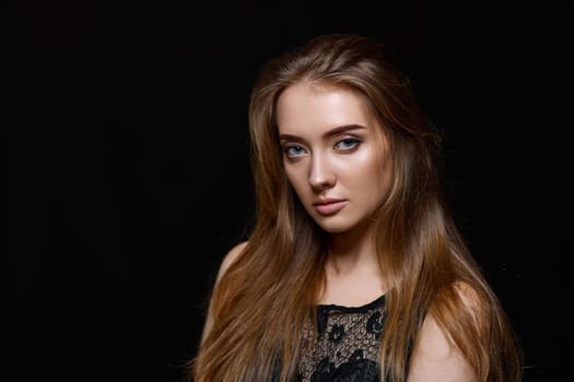 gorgeous brunette woman with long hair in black dress looking at the camera on black background. copy space
