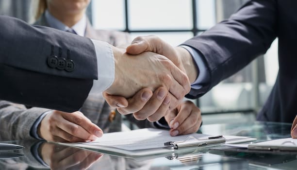 Businesspeople or lawyers shaking hands finishing up meeting or negotiation in sunny office.