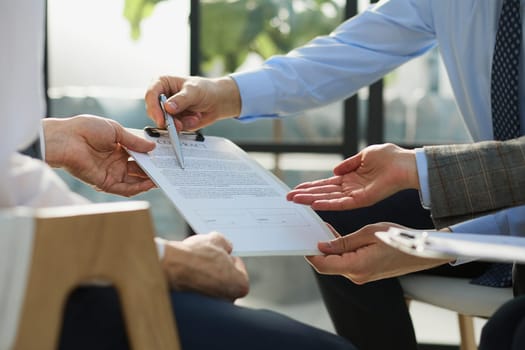 Closeup business deal meeting, businessman carefully reviewing terms and condition of contract agreement papers in office.