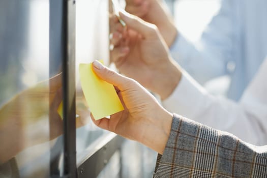 Businessman writing on sticky notes on glass wall while working in office