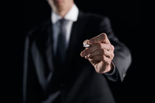 A hand holding a marker turned to the camera against a dark background