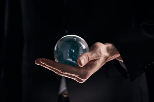 Hand holding a clear transparent crystal glass ball isolated on black background