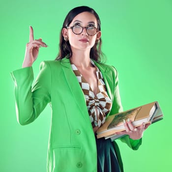 Woman, books and teacher pointing up in studio isolated on a green background. Gen z, education and emoji gesture of smart female educator carrying textbooks for learning, studying and knowledge