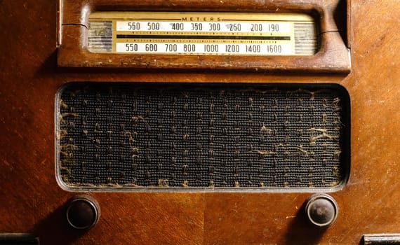 This old-fashioned antique radio made of wood clearly shows the passage of time. It features a speaker, dials, and rusty knobs.
