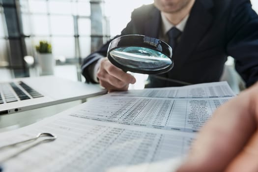 Businessman looking through a magnifying glass to document close-up