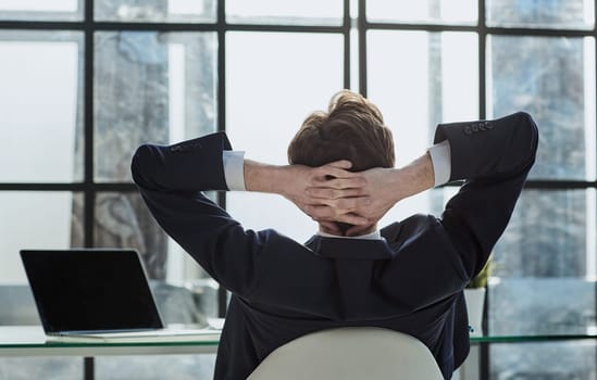 the worker sits in the office with his hands behind his head and looks out the window