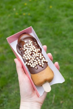 Festival Street Food Penis Shaped Waffle On Wooden Stick With Dark Chocolate, Decorated With White Air Corn Balls In Paper Box In Human Hand Outdoor. Sweet Cookie Vertical Plane.