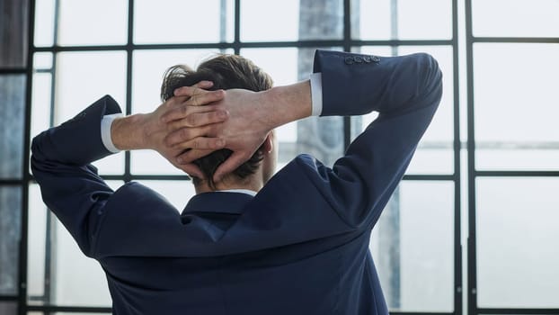 the worker sits in the office with his hands behind his head and looks out the window