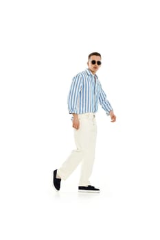 Young fashionable guy in trendy sunglasses, blue striped shirt and trousers isolated on white background. full length.