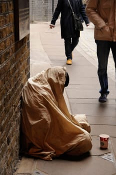 Side view of beggar homeless covered with a blanket sitting on pavement in cold weather.