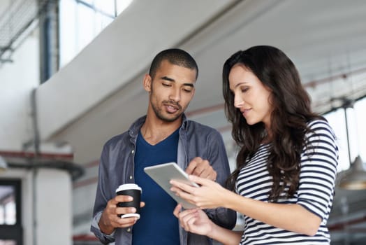 Using technology as a tool in the workplace. two coworkers standing in an office looking at a digital tablet