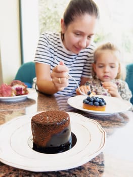 Mom feeds a little girl a blueberry tart with a fork from a plate in a cafe. High quality photo