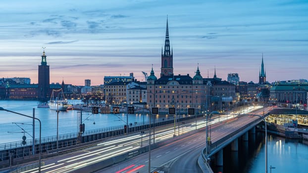 Photo of Light trails on a bridge to Stockholm at night. Silhouettes of old town against clear evening sky. Long exposure urban cityscape