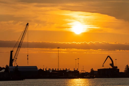 Photo of Port cranes at sunset. Cargo transportation and cargo ships.