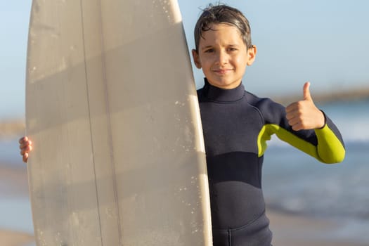 Cute little boy surfer showing a thumb up. Mid shot